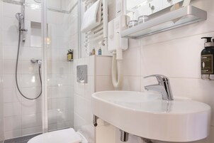 Ett modernt badrum med en dusch som är avskärmad med glasväggar, en vit tvättställ med ett kromfärgat blandare och en spegel ovanför tvättstället.