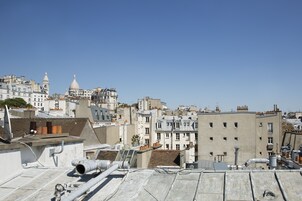 A cityscape with a variety of building styles, including a prominent dome structure and multiple rooftops with visible pipes and antennas.