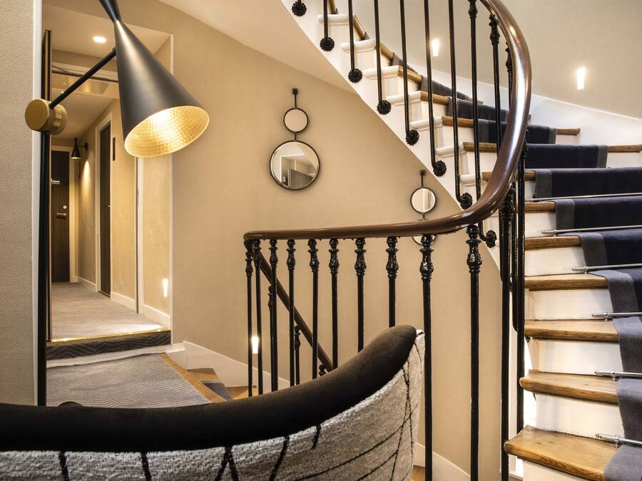 A spiral staircase with wooden steps and black balusters, a wall-mounted mirror, and a pendant light with a textured shade.