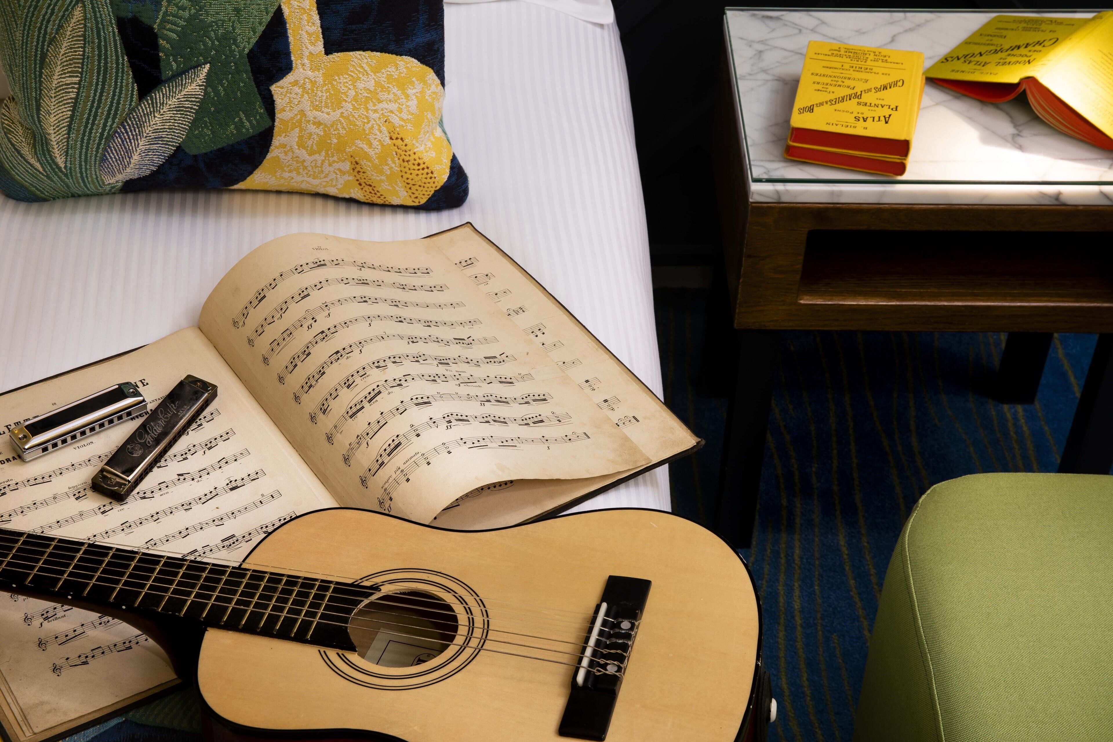 An open book with sheet music, a guitar, and harmonica on a bed.