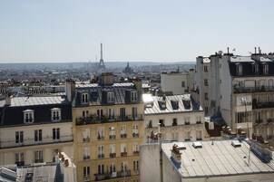 A cityscape with the Eiffel Tower in the background, featuring multi-story buildings with balconies and varied rooflines.
