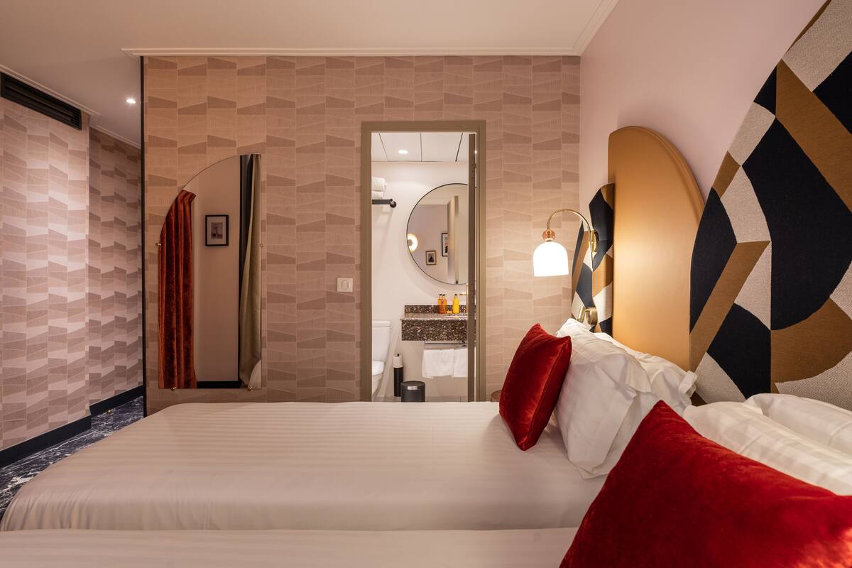 A hotel room with a large bed, a bathroom visible through an open door, and a modern wall design.