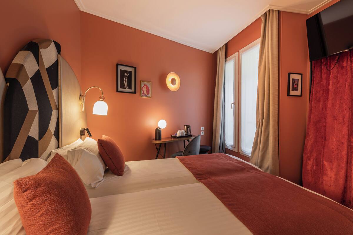 A hotel room with a bed, pillows, a desk with a lamp, a chair, and a TV.