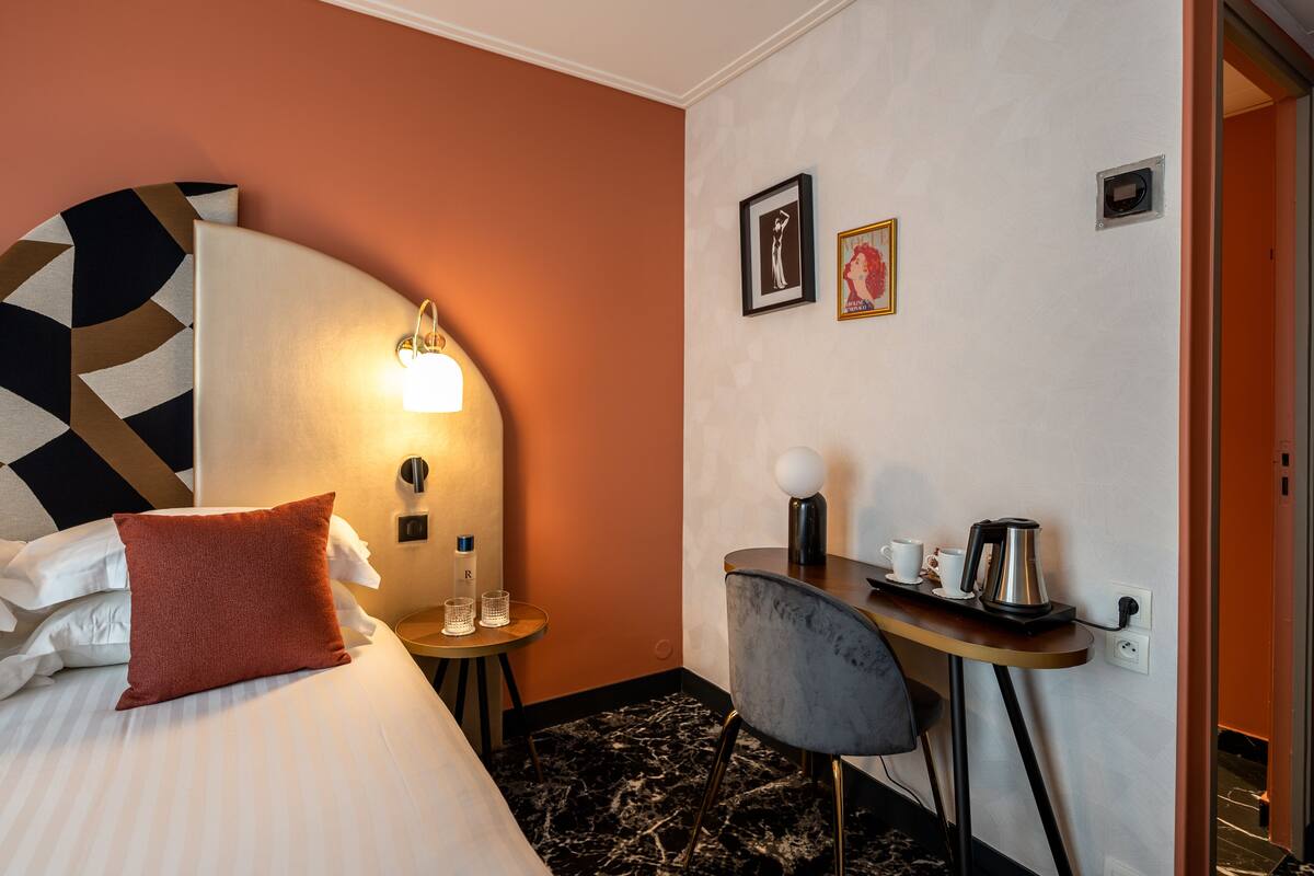 A hotel room with a bed, a desk with a chair, a lamp, and a coffee maker.