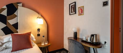 A hotel room with a bed, a desk with a chair, a lamp, and a coffee maker.
