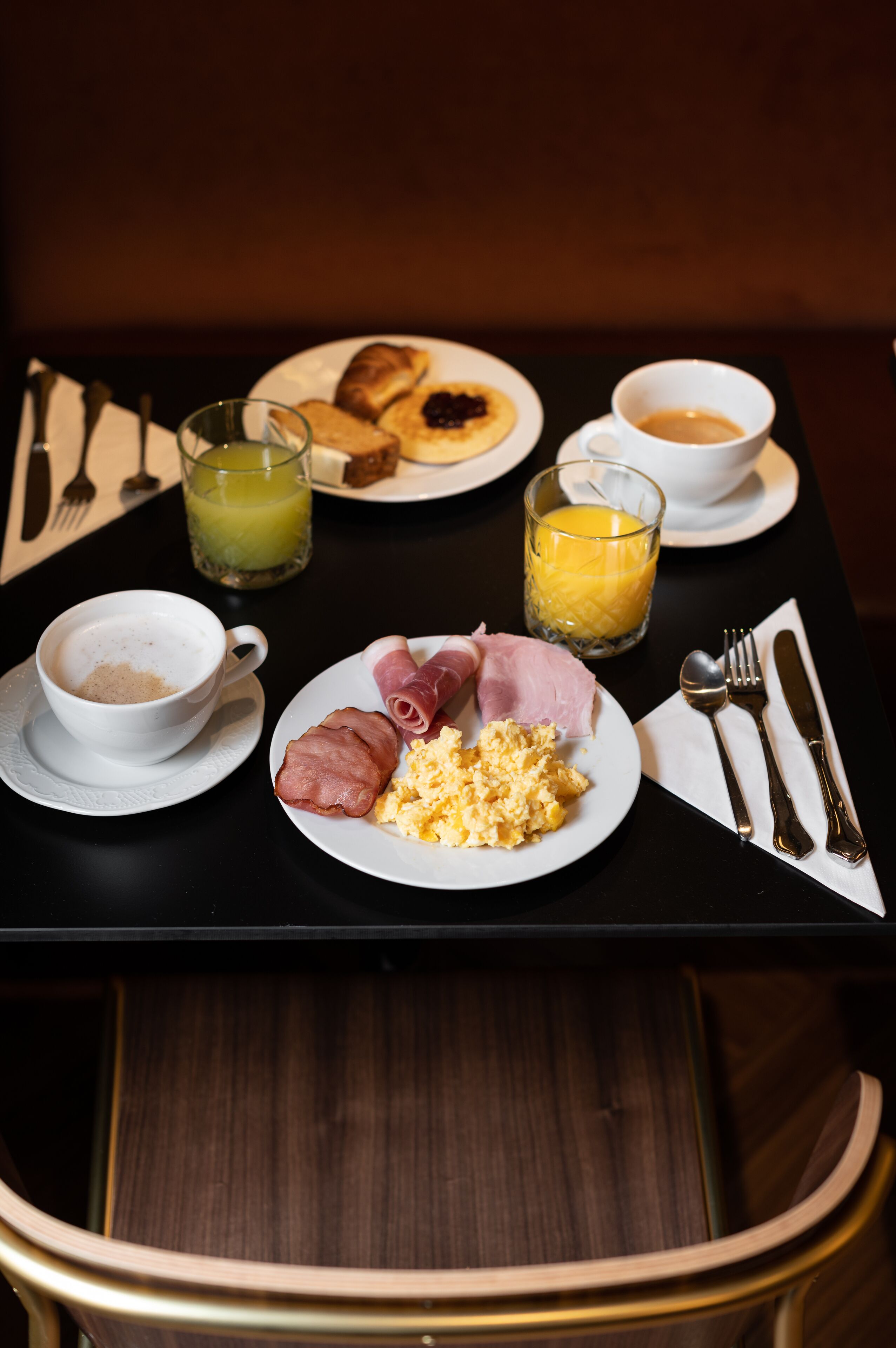 A breakfast table with plates of food, a cup of coffee, and two glasses of juice.