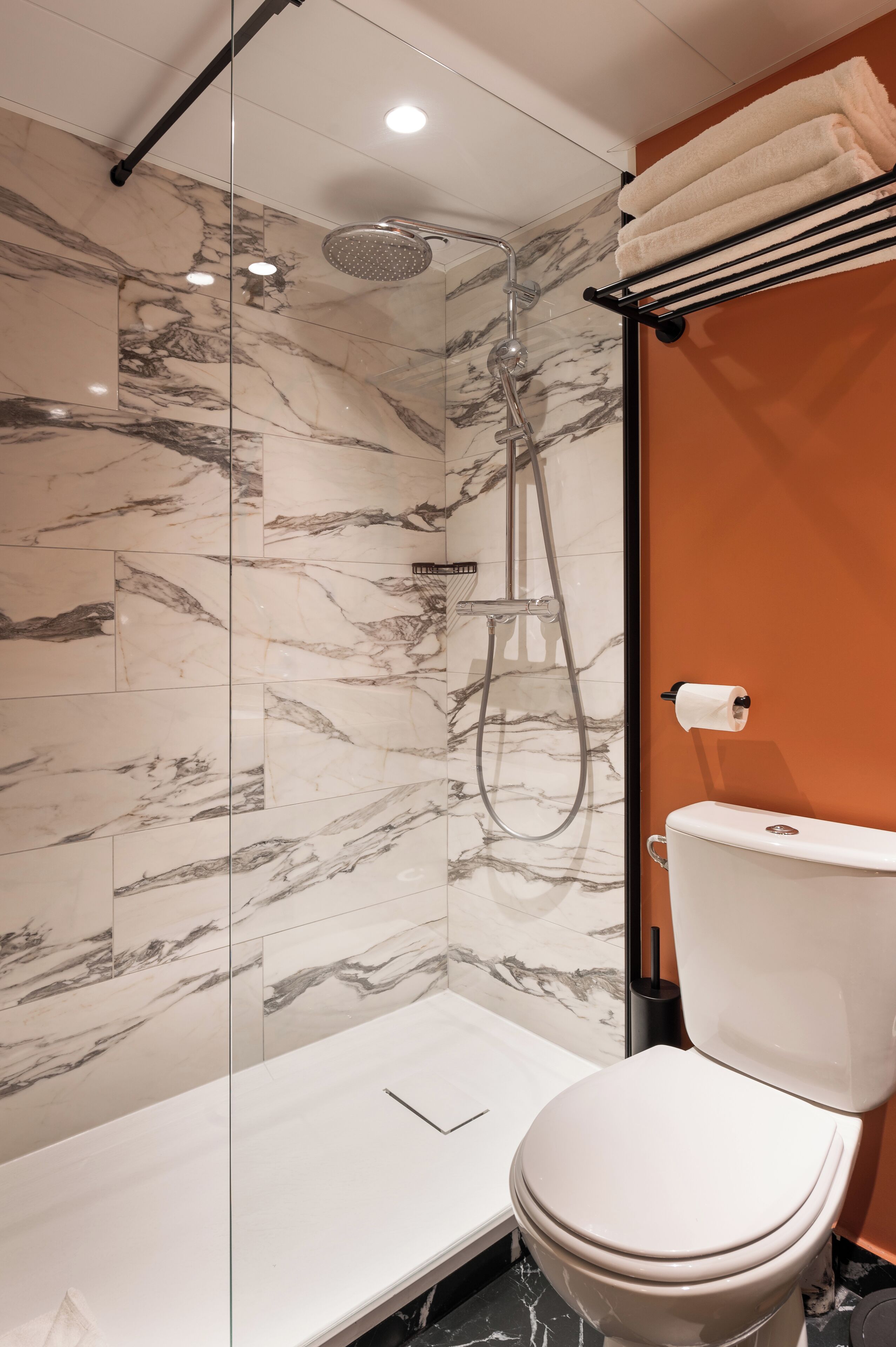 Un baño moderno con ducha de vidrio, azulejos de mármol, un inodoro blanco y un perchero para toallas.
