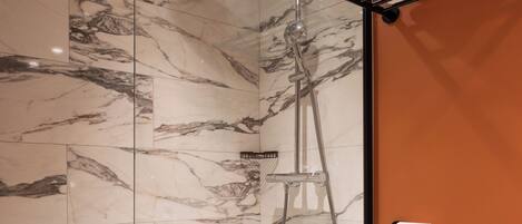 Un baño moderno con ducha de vidrio, azulejos de mármol, un inodoro blanco y un perchero para toallas.