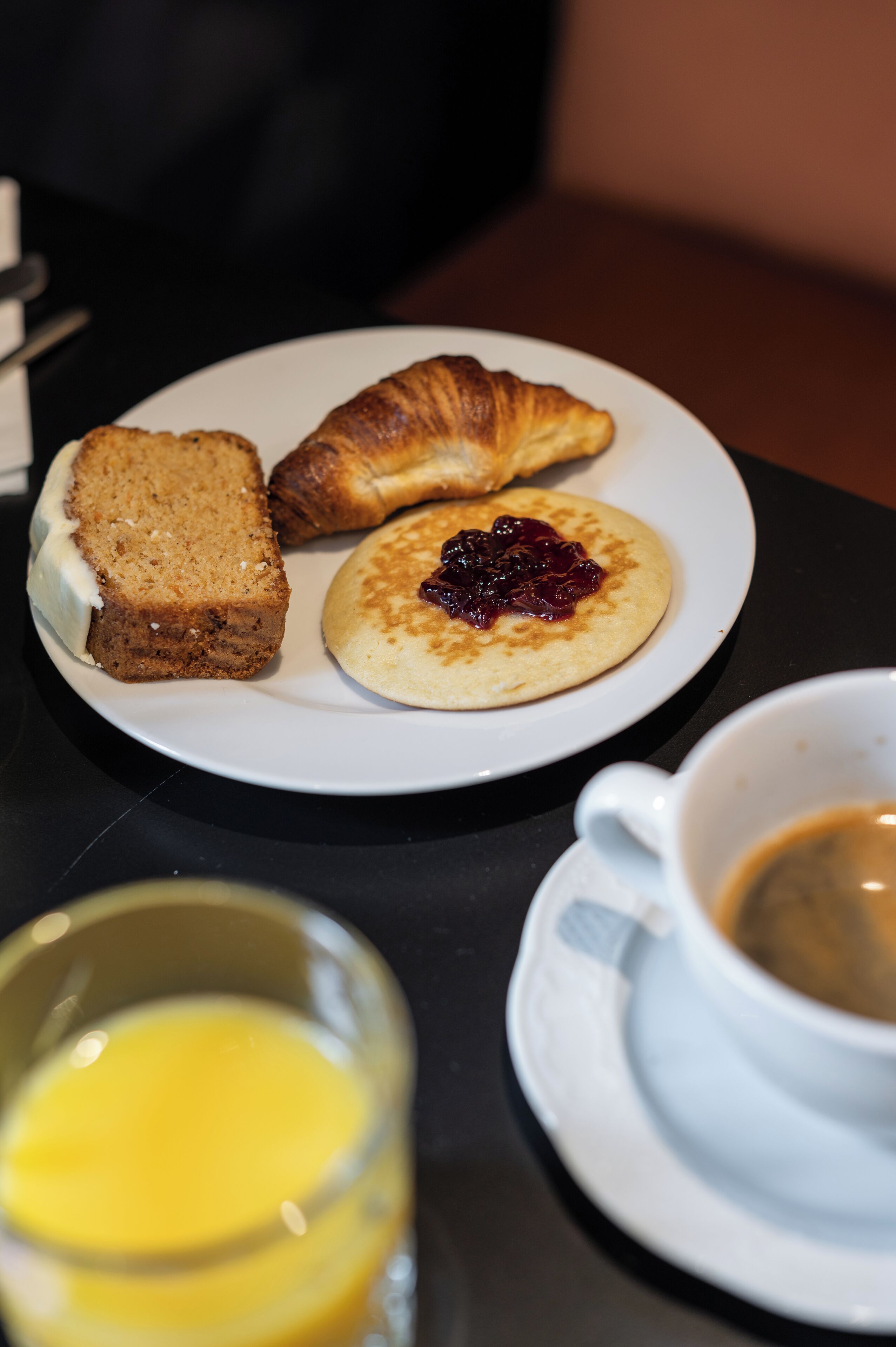 Een ontbijtbord met een croissant, een sneetje brood, pannenkoeken met jam en een kop koffie.