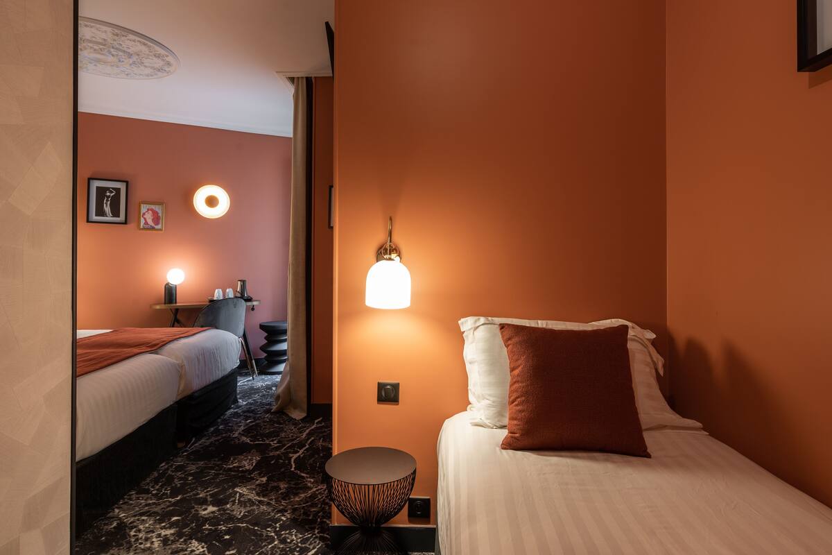 A hotel room with a bed, a round side table, a lamp, and a wall-mounted light fixture.