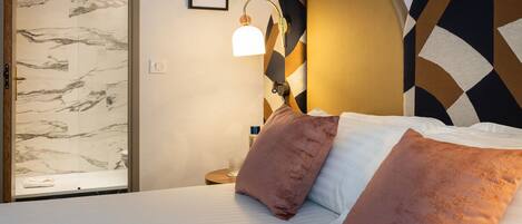 Habitación de hotel con cama, mesita de noche, lámpara, un cuadro enmarco y una puerta con diseño de mármol.