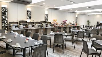 Un comedor moderno con varias mesas y sillas, una barra de buffet con comida y bebidas, y un interior limpio y bien iluminado.