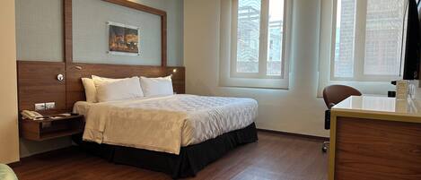 Una habitación de hotel con cama, mesita de noche, lámpara y escritorio con silla.