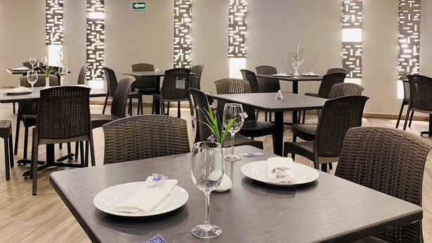 Un'elegante sala da pranzo moderna con tavoli in legno scuro e sedie in vimini, con una parete decorativa caratterizzata da motivi geometrici e illuminazione a incasso.