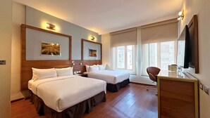 Una camera d'albergo con due letti, una scrivania e una televisione.