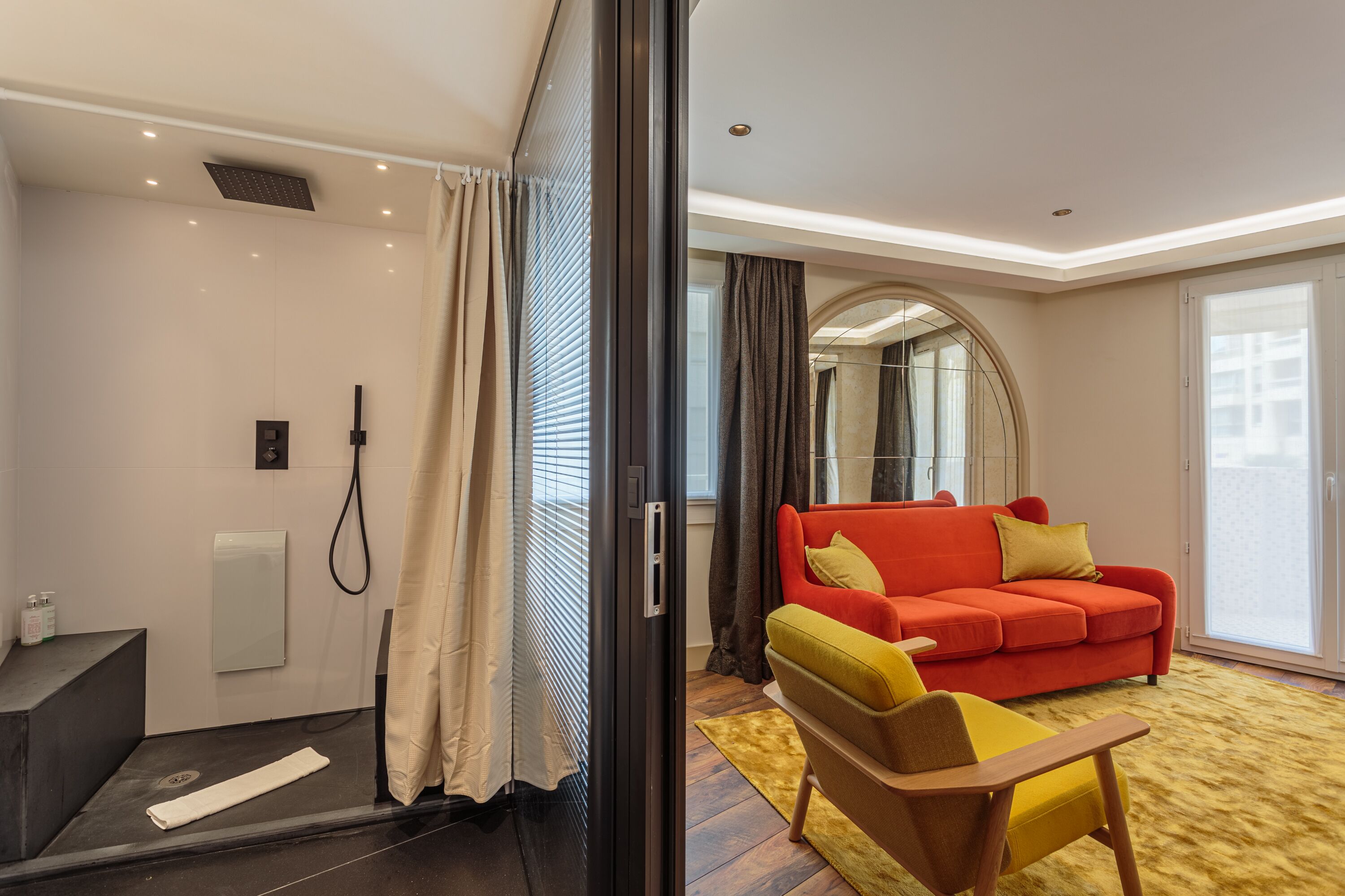 A modern hotel room with a shower, a red sofa, and a yellow armchair.