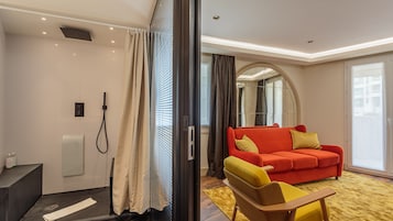 Een moderne hotelkamer met een douche, een rode bank en een gele fauteuil.