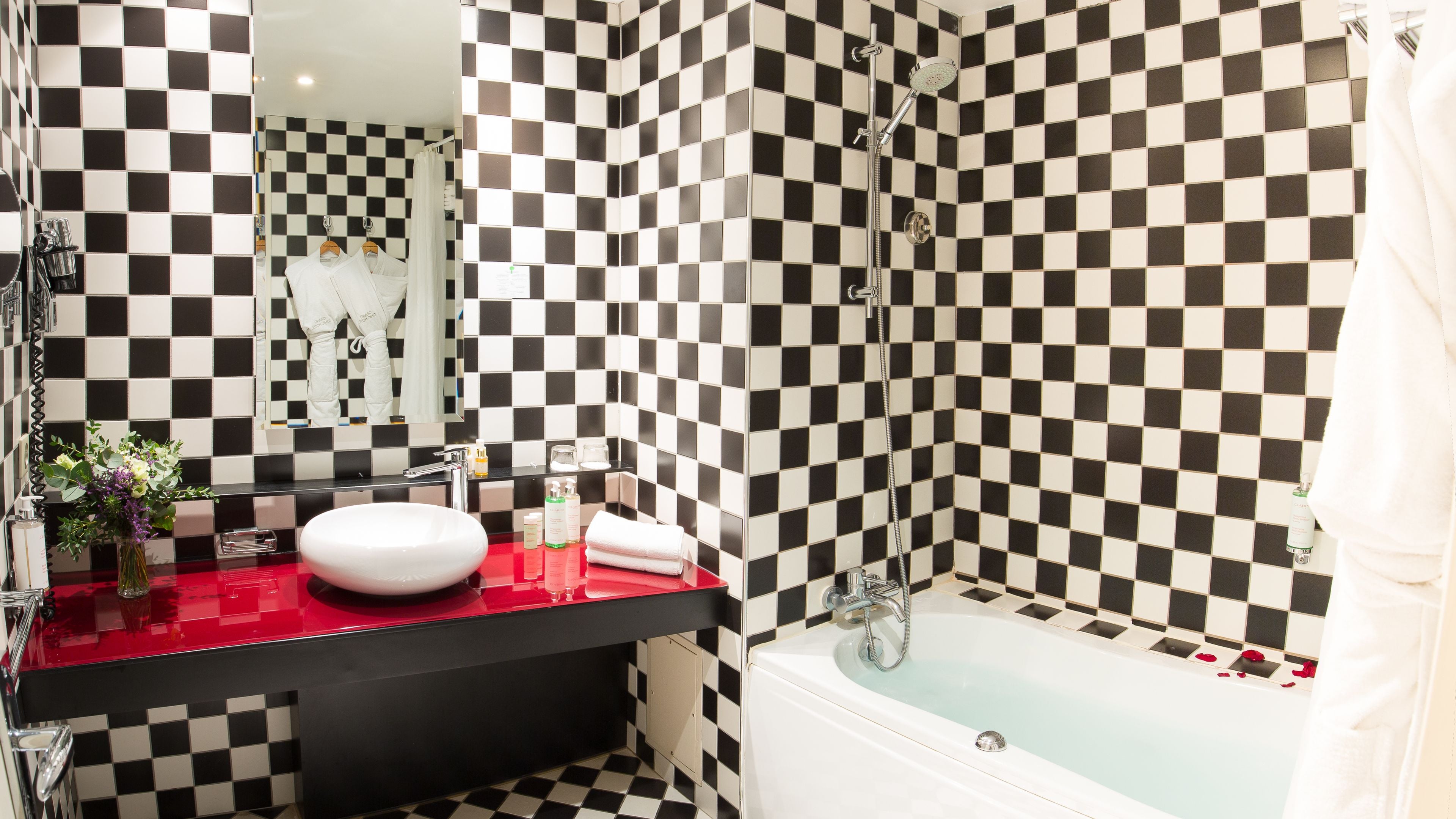 A bathroom with a checkered black and white tile wall, a red sink, and a white bathtub.