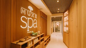 A wooden interior hallway with a sign reading "NUXE SPA PARIS" and a reception desk with bowls of fruit and cups. - Grand Tonic Hotel & SPA NUXE (Biarritz)