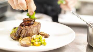 Un chef prepara un plato con bistec, patatas y maíz sobre un plato blanco.