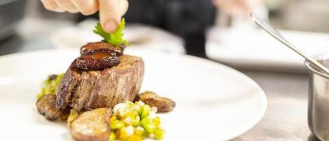 A chef preparing a dish with a steak, potatoes, and corn on a white plate.