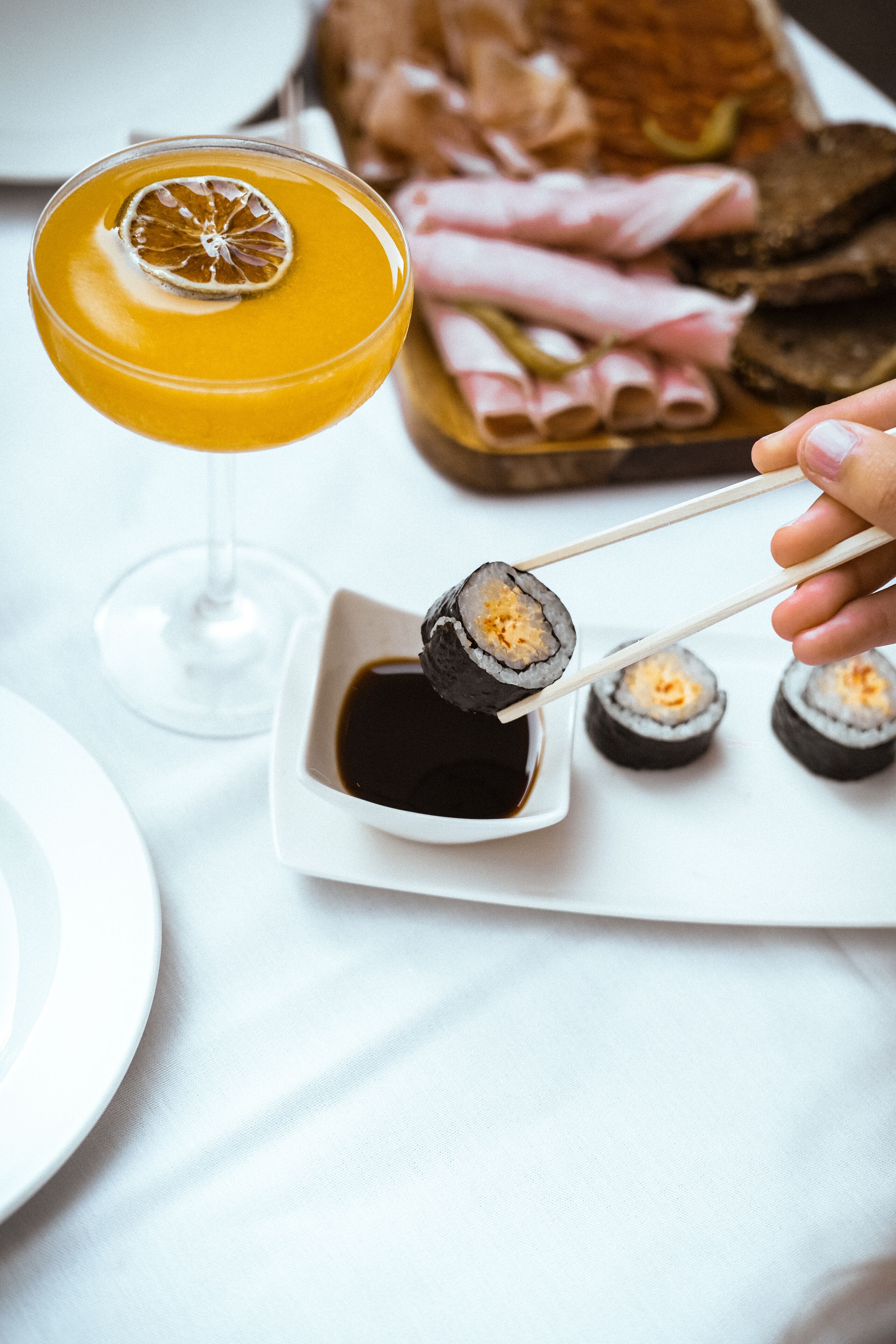 A martini glass with a lemon slice garnish, sushi on a plate, and a glass of orange juice.