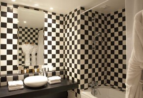 Un baño con pared de baldosas a cuadros blanco y negro, un lavamanos blanco y una bañera.