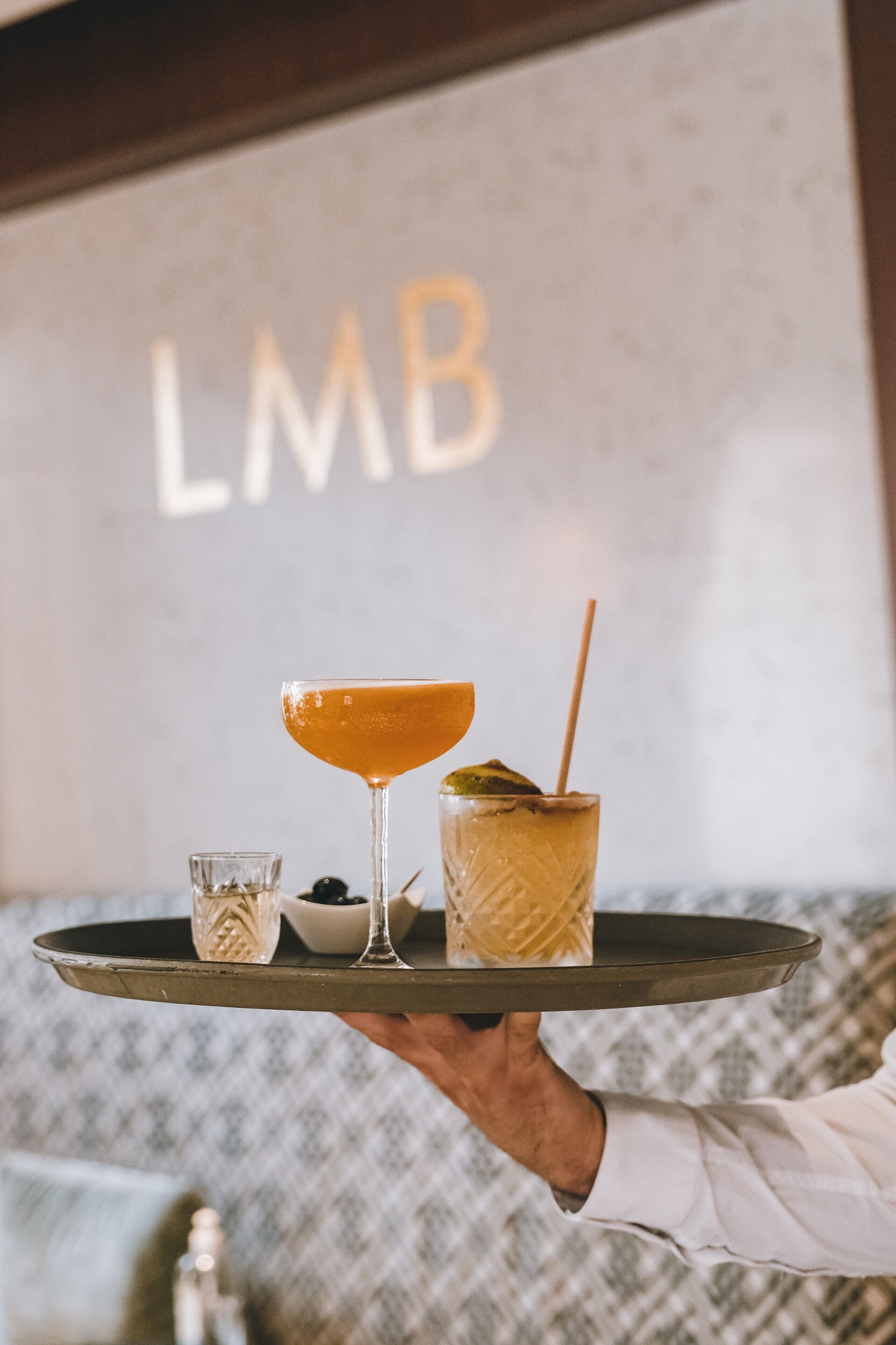 A tray with a cocktail, a glass of iced tea, and a small bowl of olives.