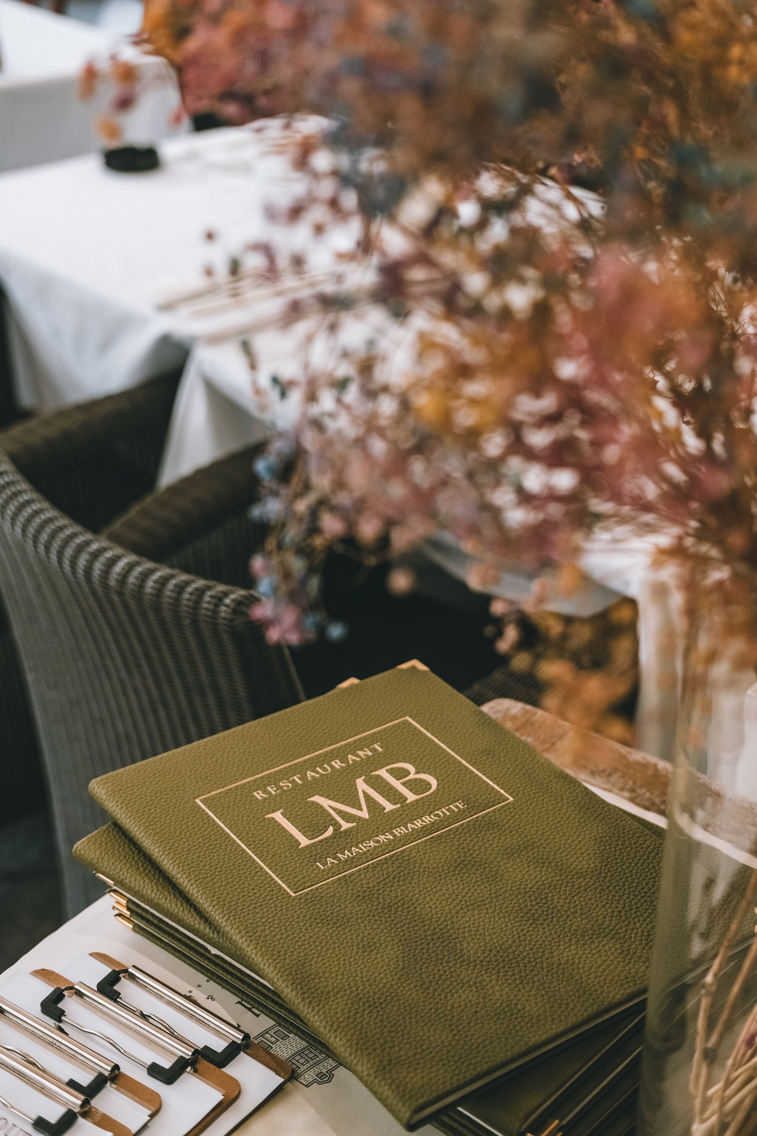 A stack of green menus with the text "RESTAURANT LMB LA MAISON BARROTTE" on a table.