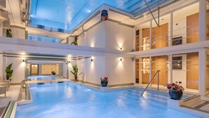 A modern indoor swimming pool with a glass ceiling, surrounded by a clean, minimalist design with a view of the sky. - Grand Tonic Hotel & SPA NUXE (Biarritz)