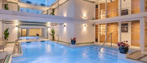 Una piscina interna moderna con soffitto in vetro, immersa in un ambiente pulito e dal design minimalista con vista sul cielo.