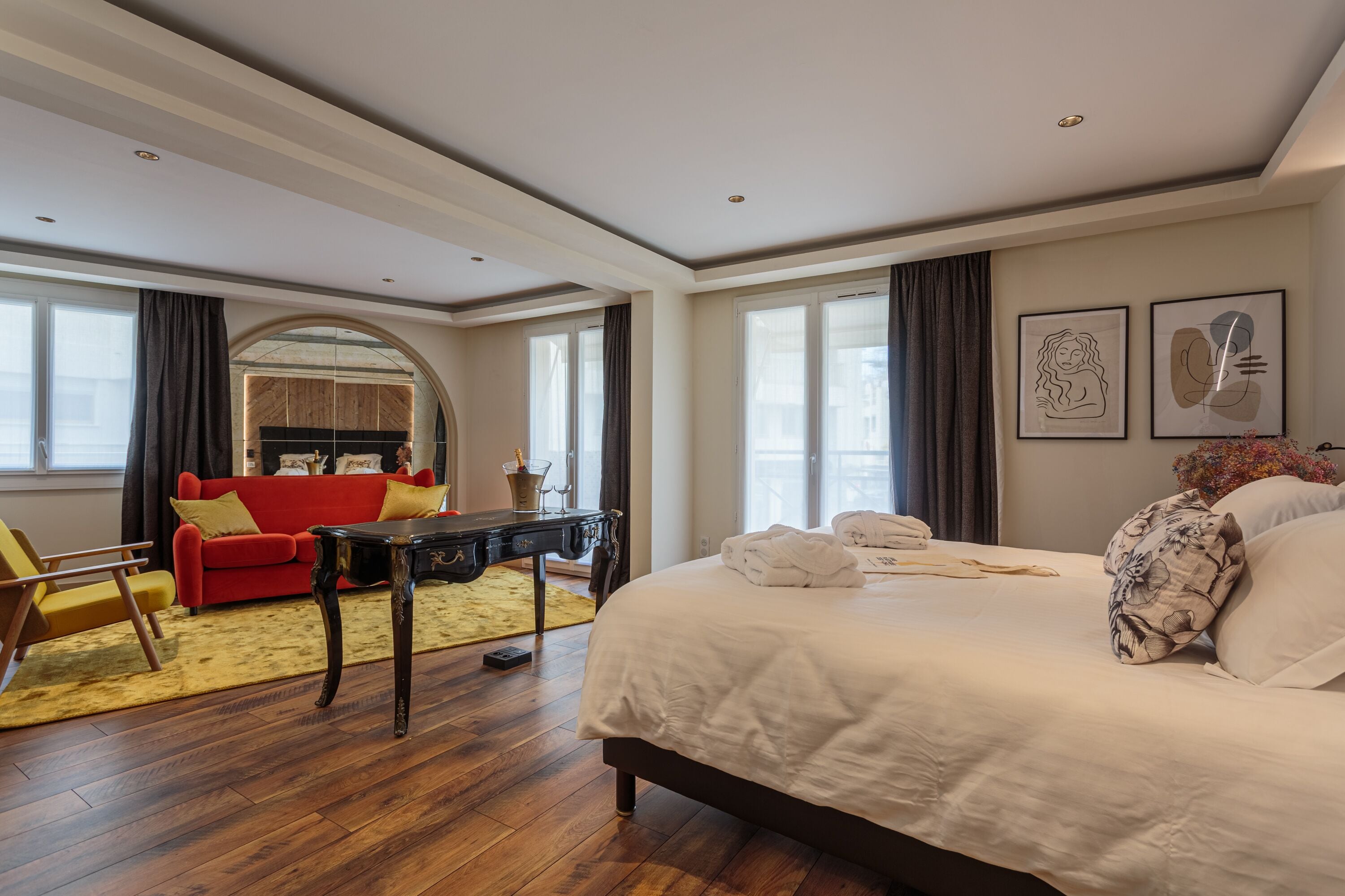 Habitación de hotel con una cama grande, un sofá rojo, una mesa de centro de madera y un espejo.