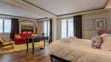 Habitación de hotel con una cama grande, un sofá rojo, una mesa de centro de madera y un espejo.