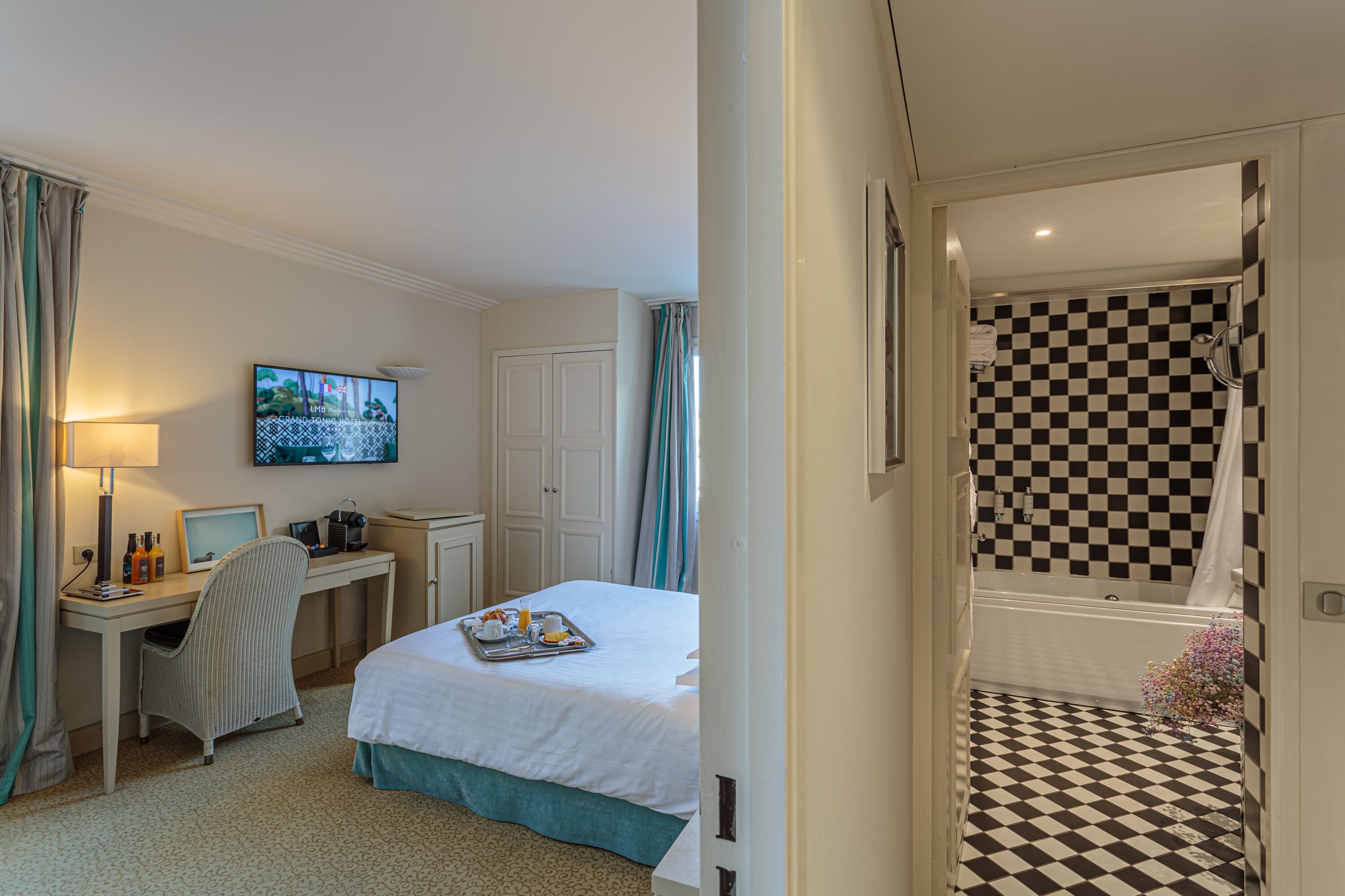 Habitación de hotel con cama, escritorio, silla y televisor en la pared.