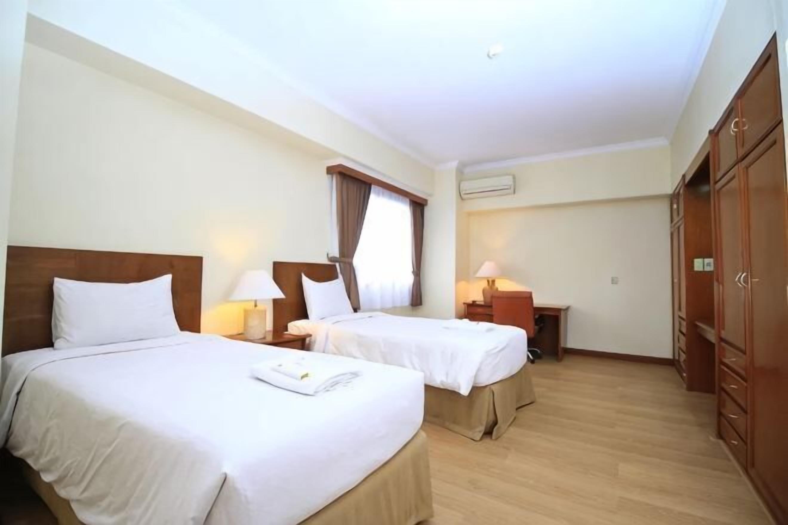 A hotel room with two beds, a desk, a wardrobe, and a window with curtains.