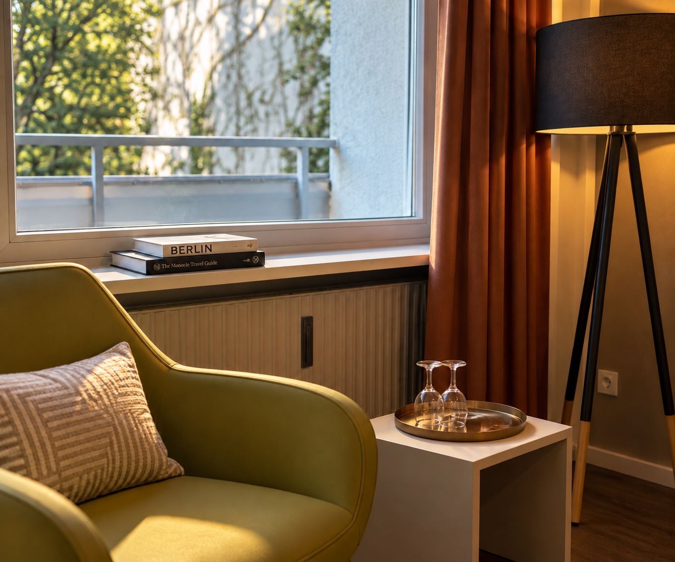 A room with a window, a chair, a bedside table with a lamp, and a tray with glasses.