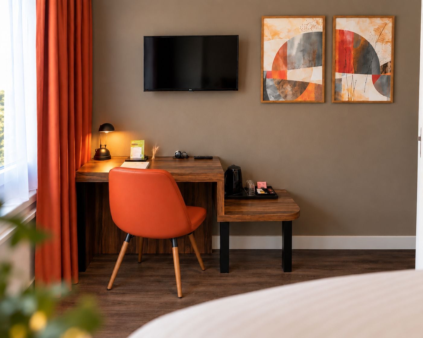 A hotel room with a desk, chair, TV, artwork, and a window with curtains.