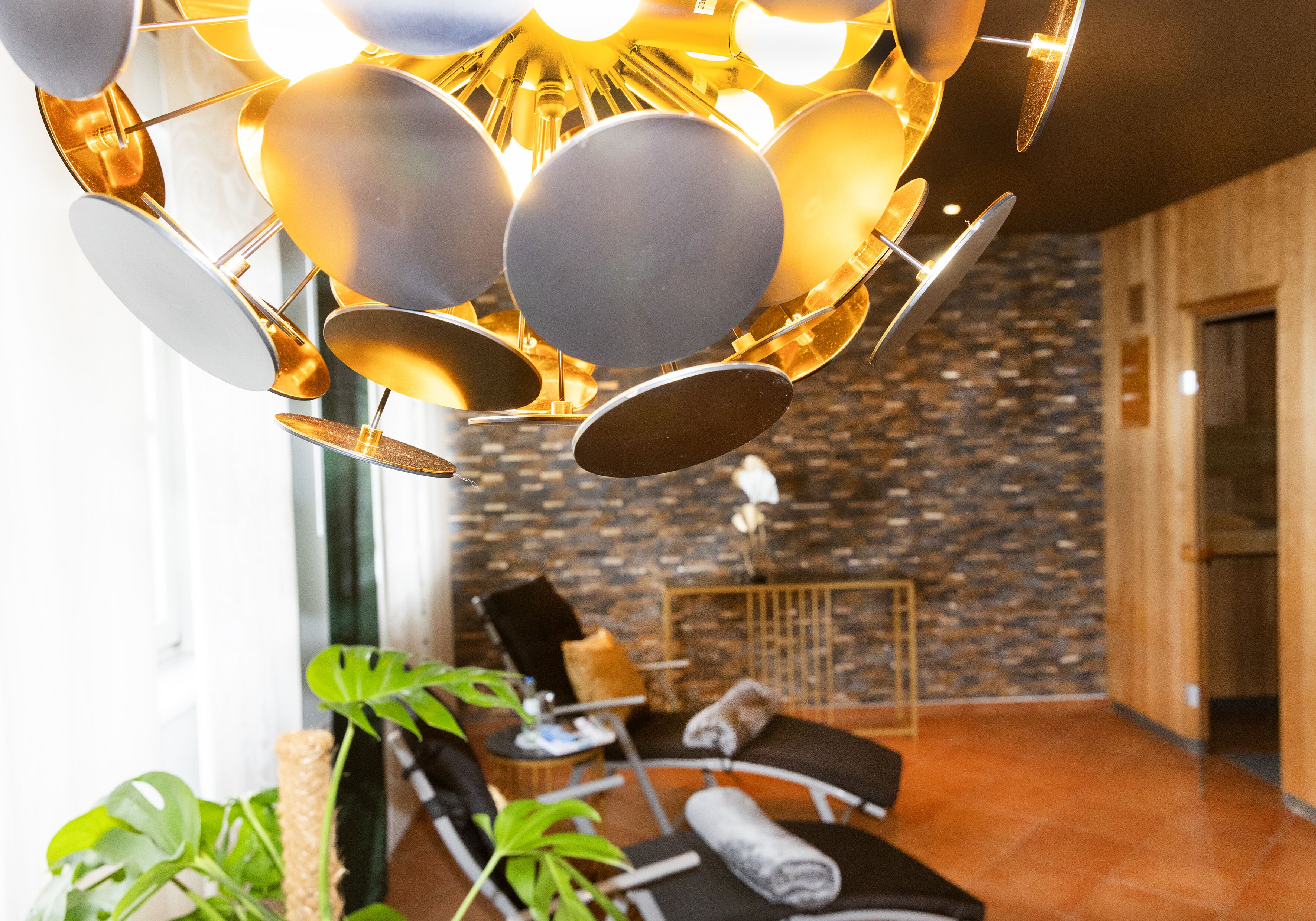 Un intérieur moderne agrémenté d’un luminaire au plafond original, d’un mur en pierre et d’un coin salon avec une plante et une serviette.