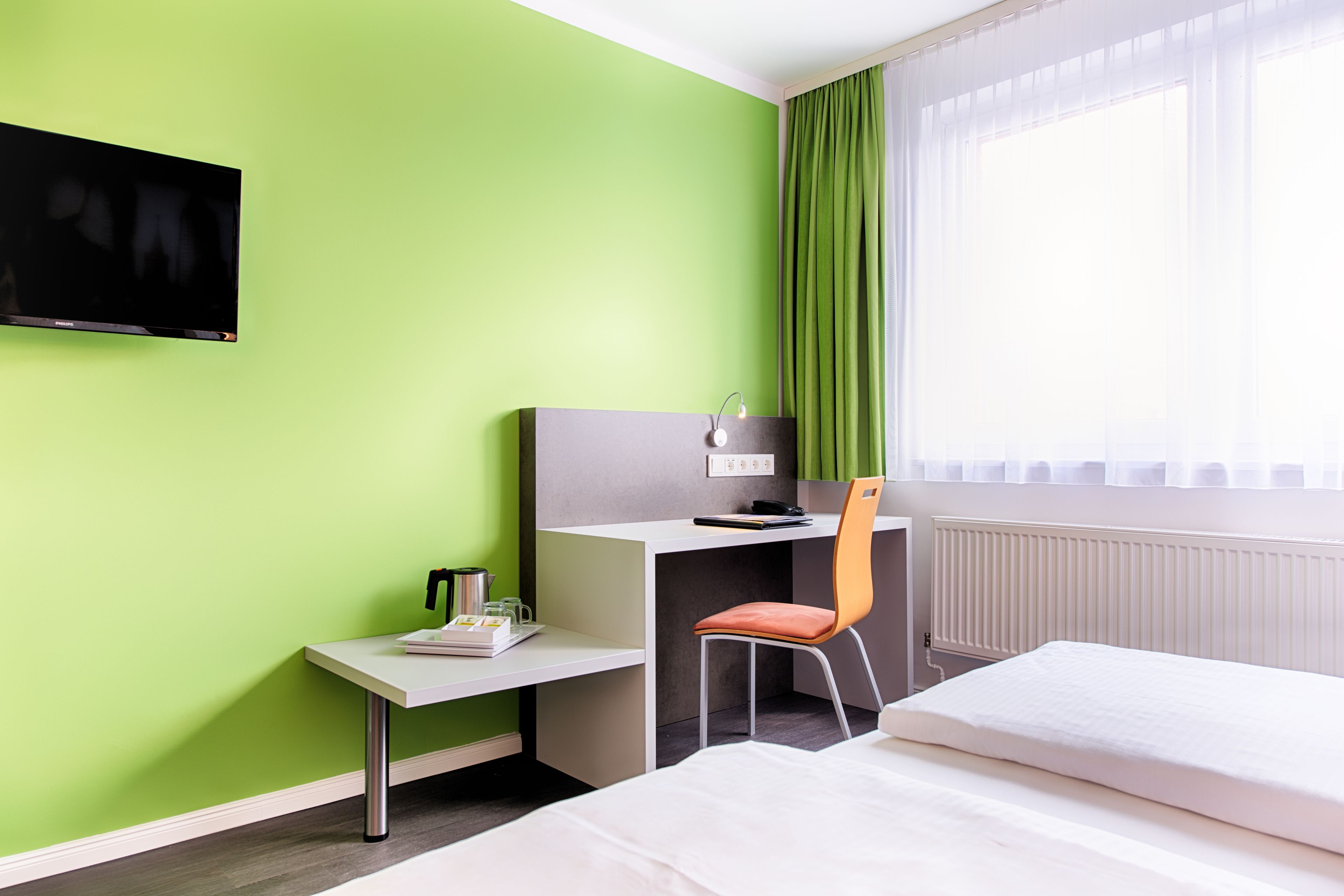 Een hotelkamer met een bed, een bureau, een stoel, een televisie en een raam met gordijnen.