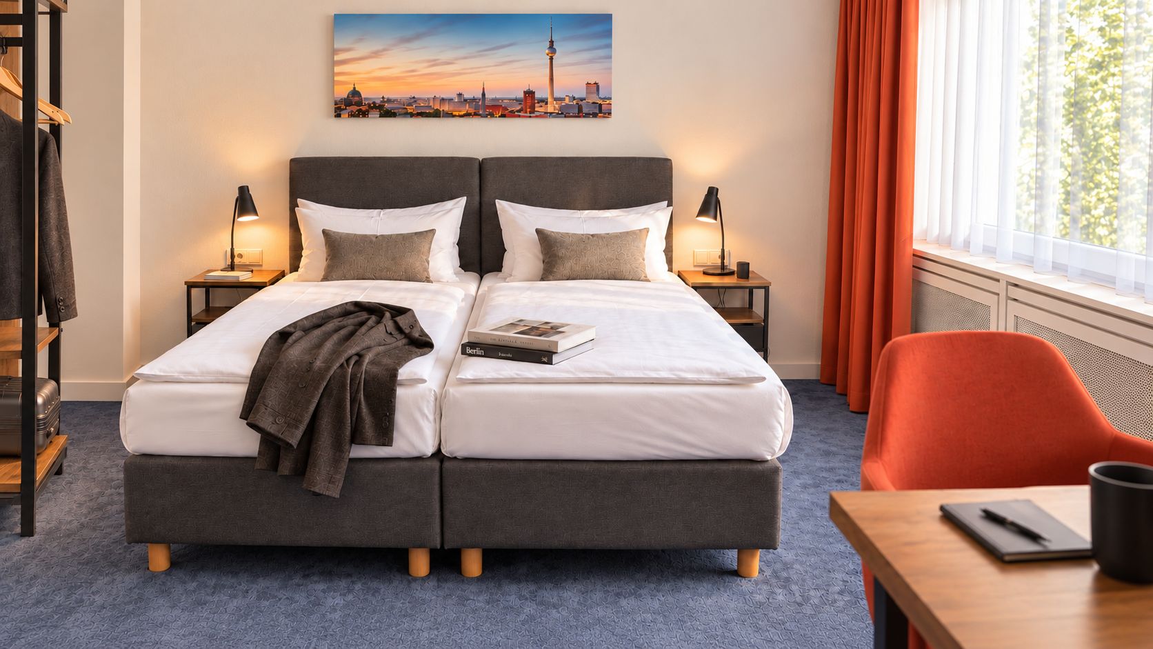 A double bed with a cityscape view, a side table with a book, and a red chair.