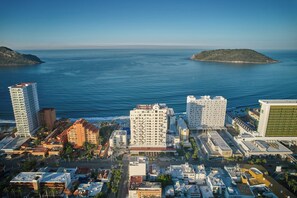 A coastal cityscape with high-rise buildings, a clear blue sea, and a small island in the distance.