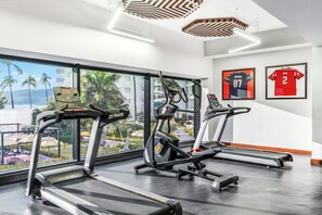 A gym with treadmills, exercise bikes, and a large window with a view of palm trees and buildings.