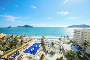 Un resort con zona de piscina, palmeras y vistas al mar.