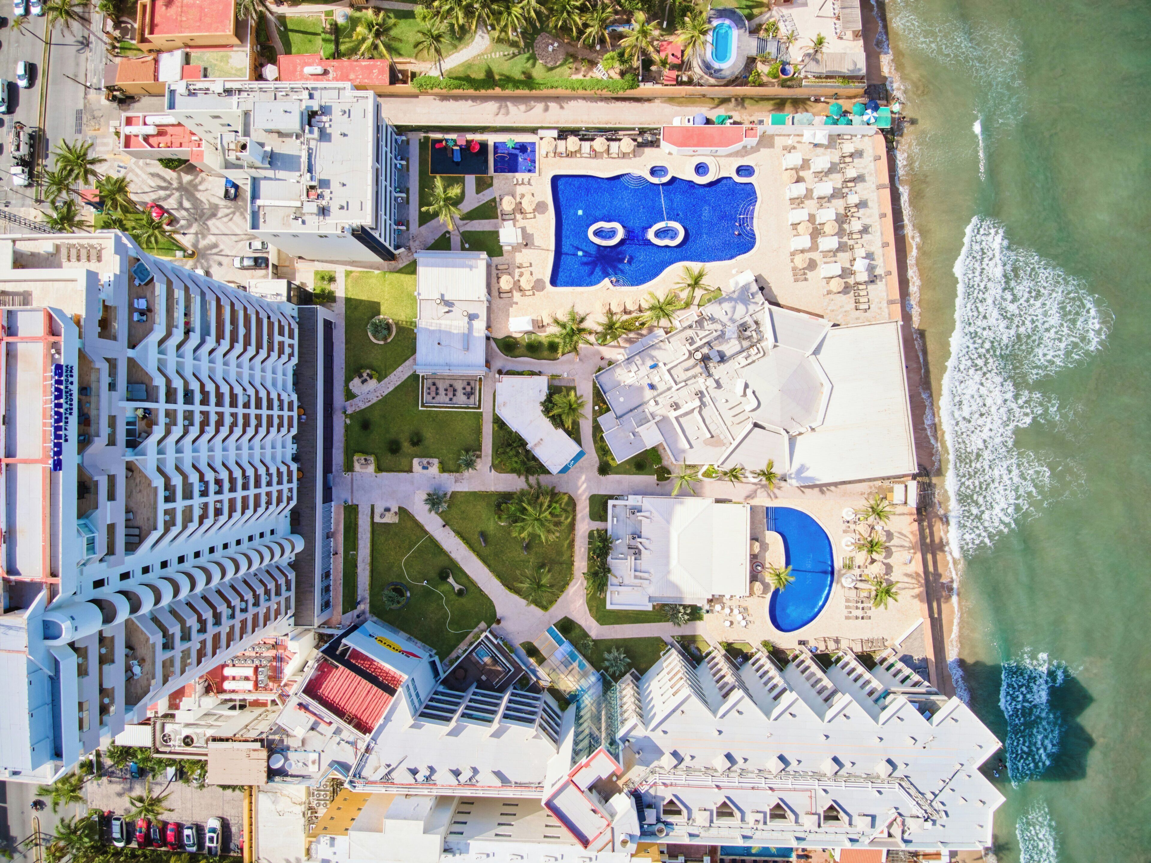 An aerial view of a resort with multiple swimming pools, a beach area, and a parking lot.