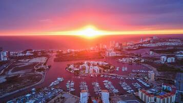 An aerial view of a marina with boats docked, surrounded by buildings and a sunset in the background.