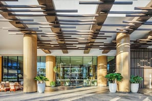 A modern lobby with large columns, a glass entrance, and potted plants.