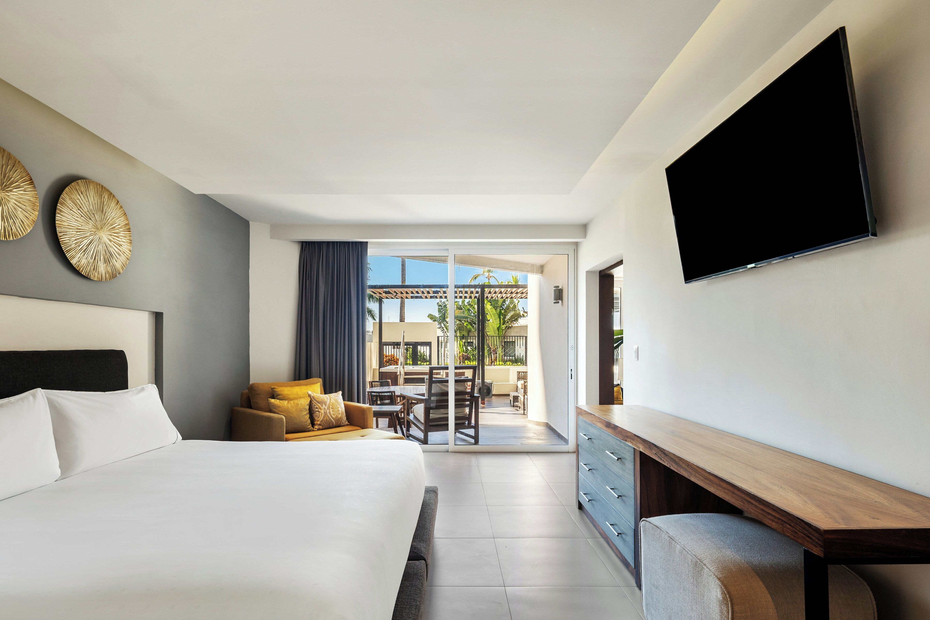A modern hotel room with a large bed, a flat-screen TV, and a view of the outdoor patio.