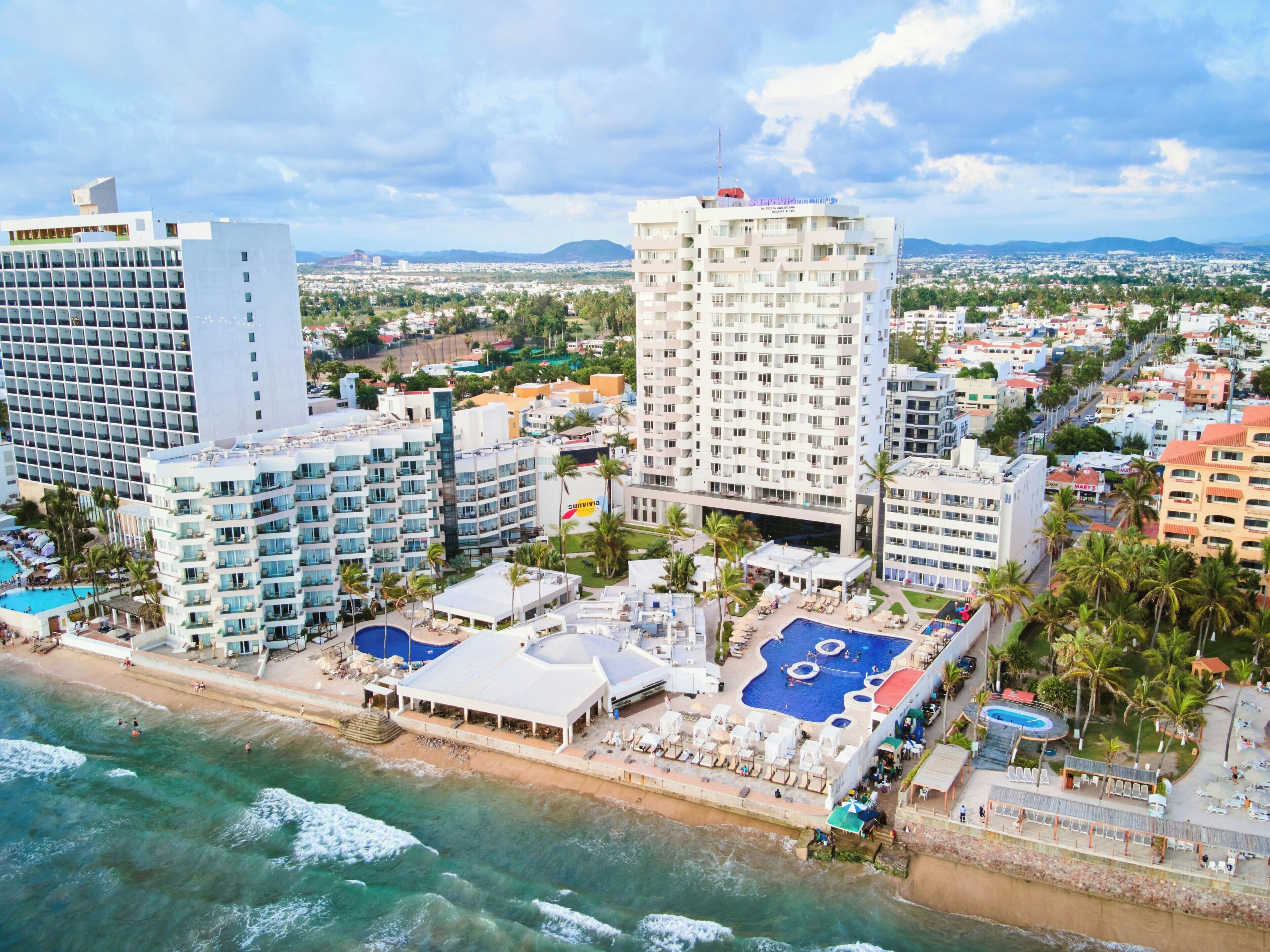 Un hotel costero con varias edificaciones, acceso directo a la playa y una zona de piscina.