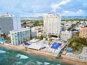 Un hotel costero con varias edificaciones, acceso directo a la playa y una zona de piscina.