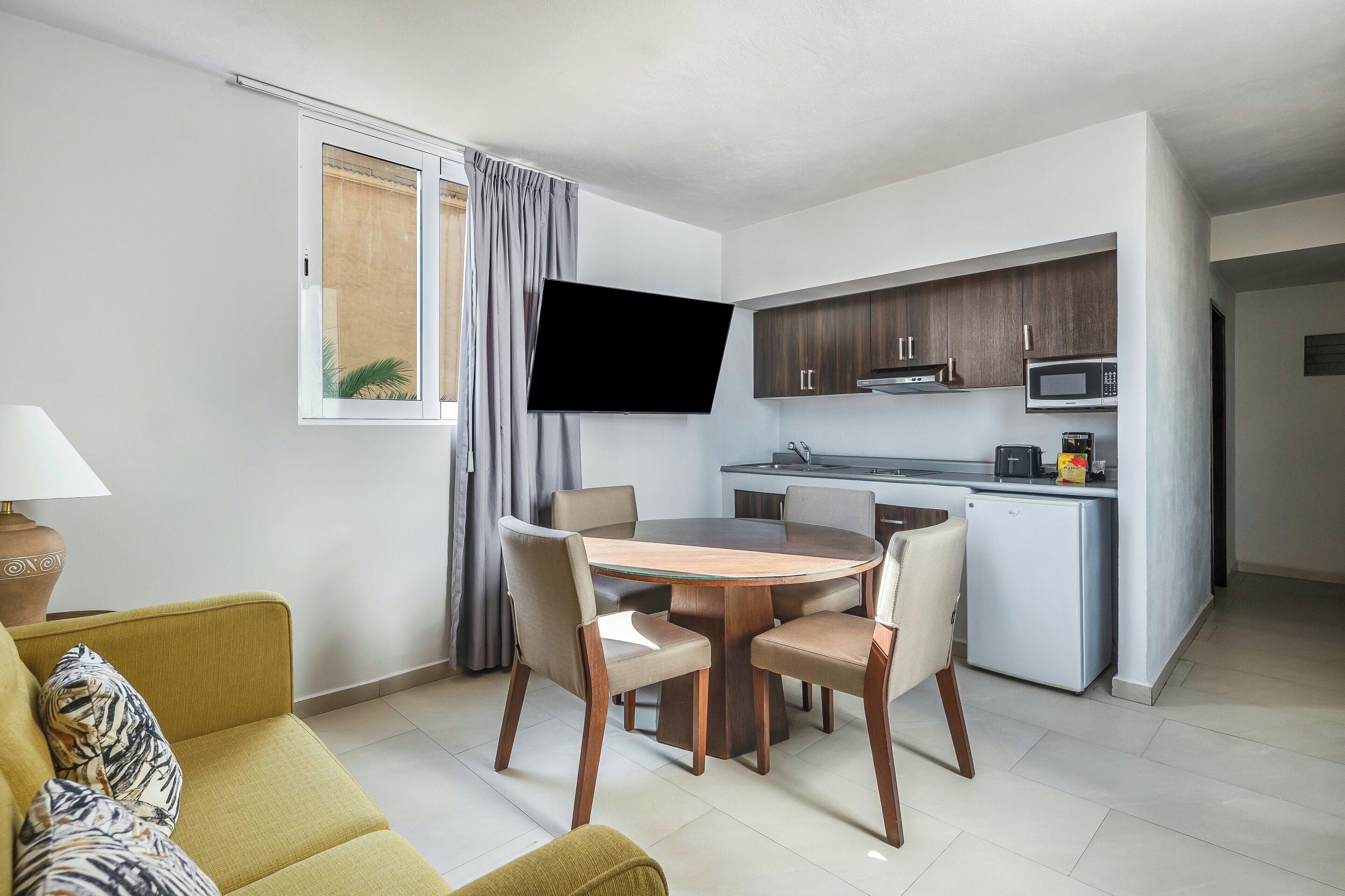 Un espace de vie compact comprenant un coin repas, une kitchenette et un téléviseur fixé au mur.